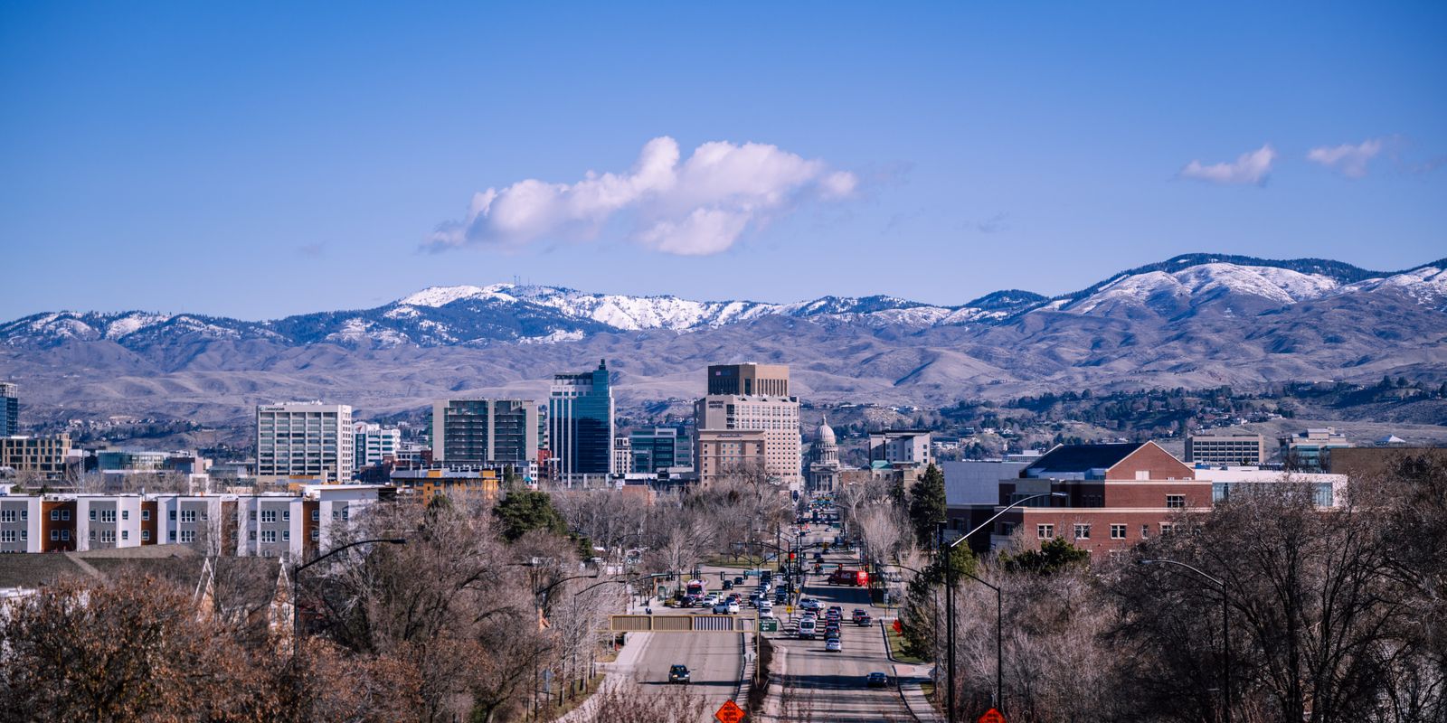 Downtown Boise office towers and a tree-lined avenue below snow-dusted foothills on a clear day.