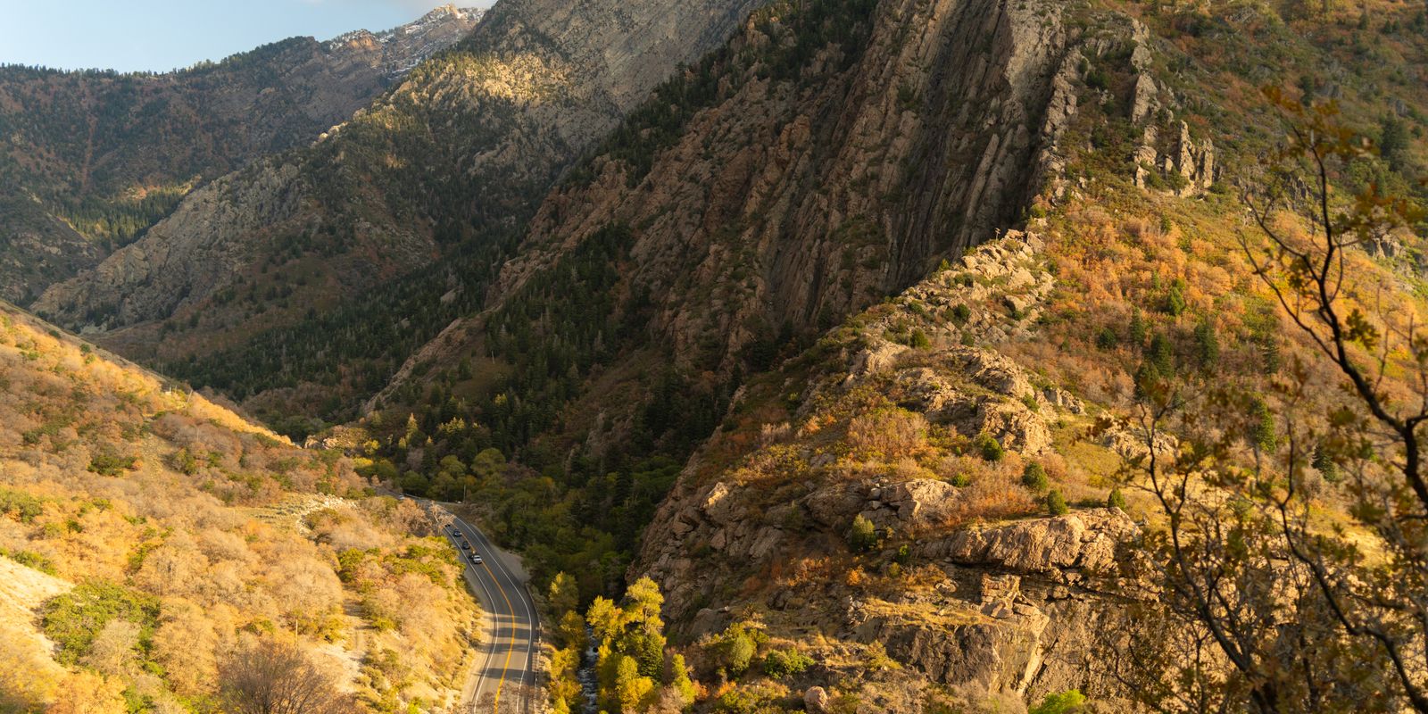 A narrow road winding up Big Cottonwood Canyon between steep cliffs and slopes of orange and yellow autumn scrub.