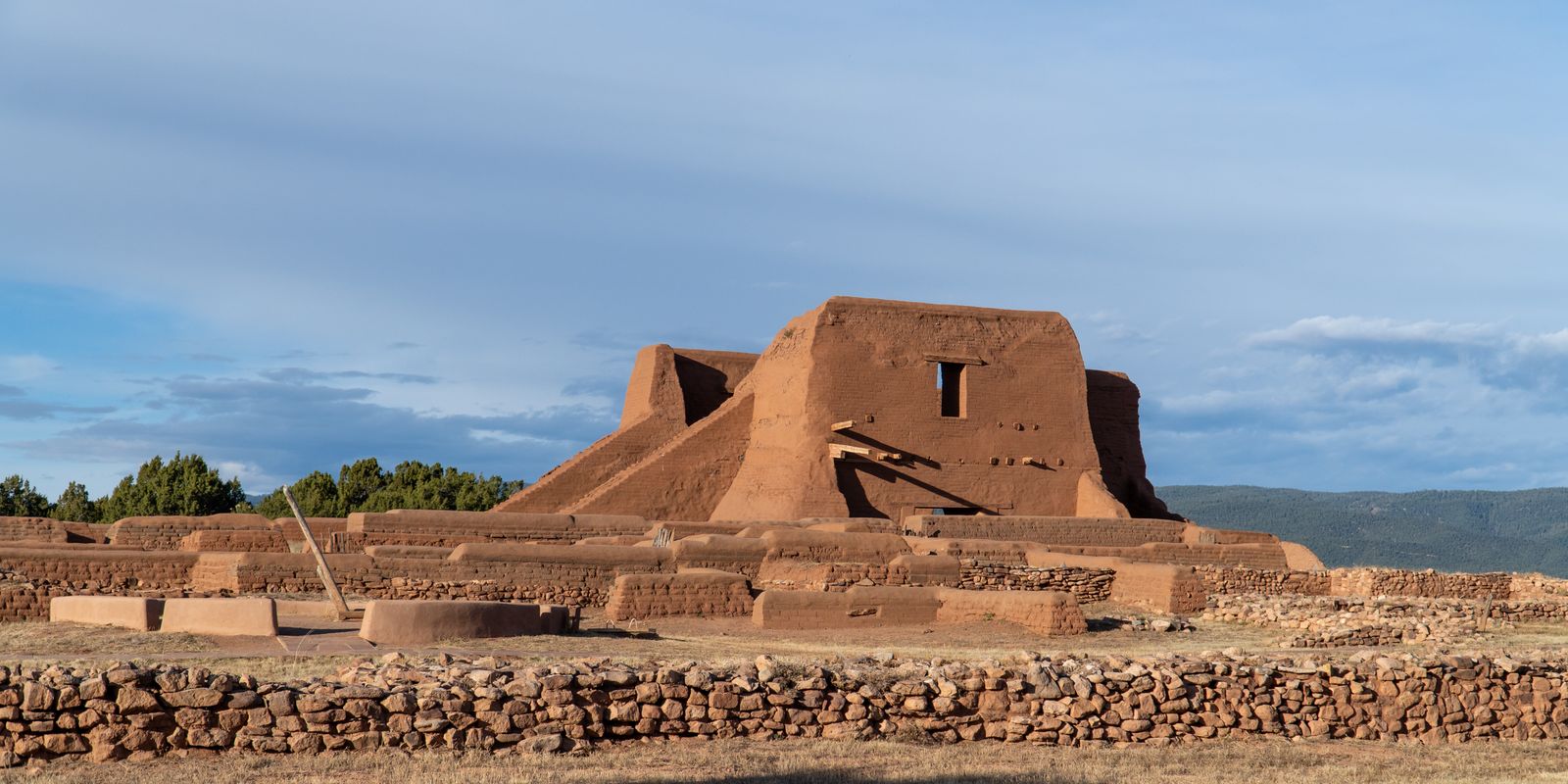 Ruined adobe mission church and low stone walls under a wide sky at Pecos National Historical Park, New Mexico.