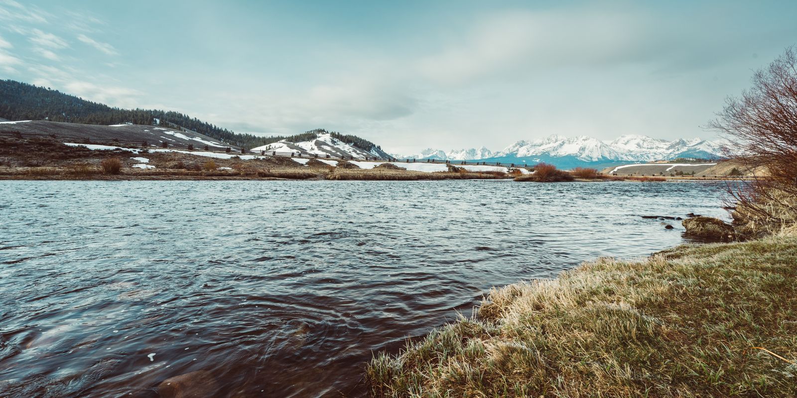 A wide river with frosty grass on the bank and snowy mountains on the horizon at Stanley, Idaho