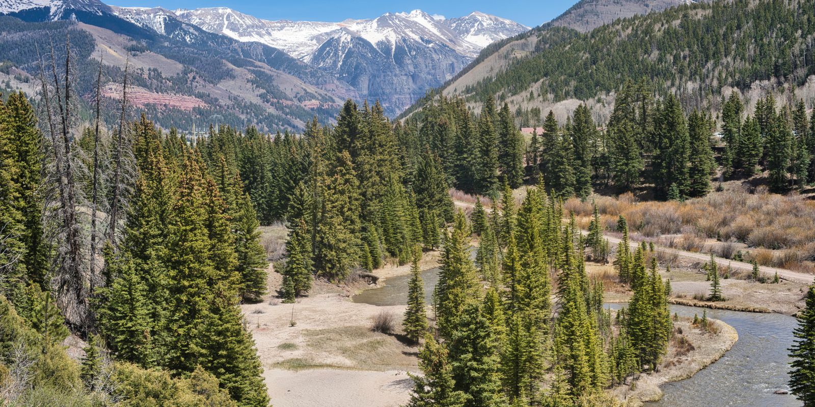 A river winding through pine forest below snow-capped peaks in the San Juan Mountains of Colorado.