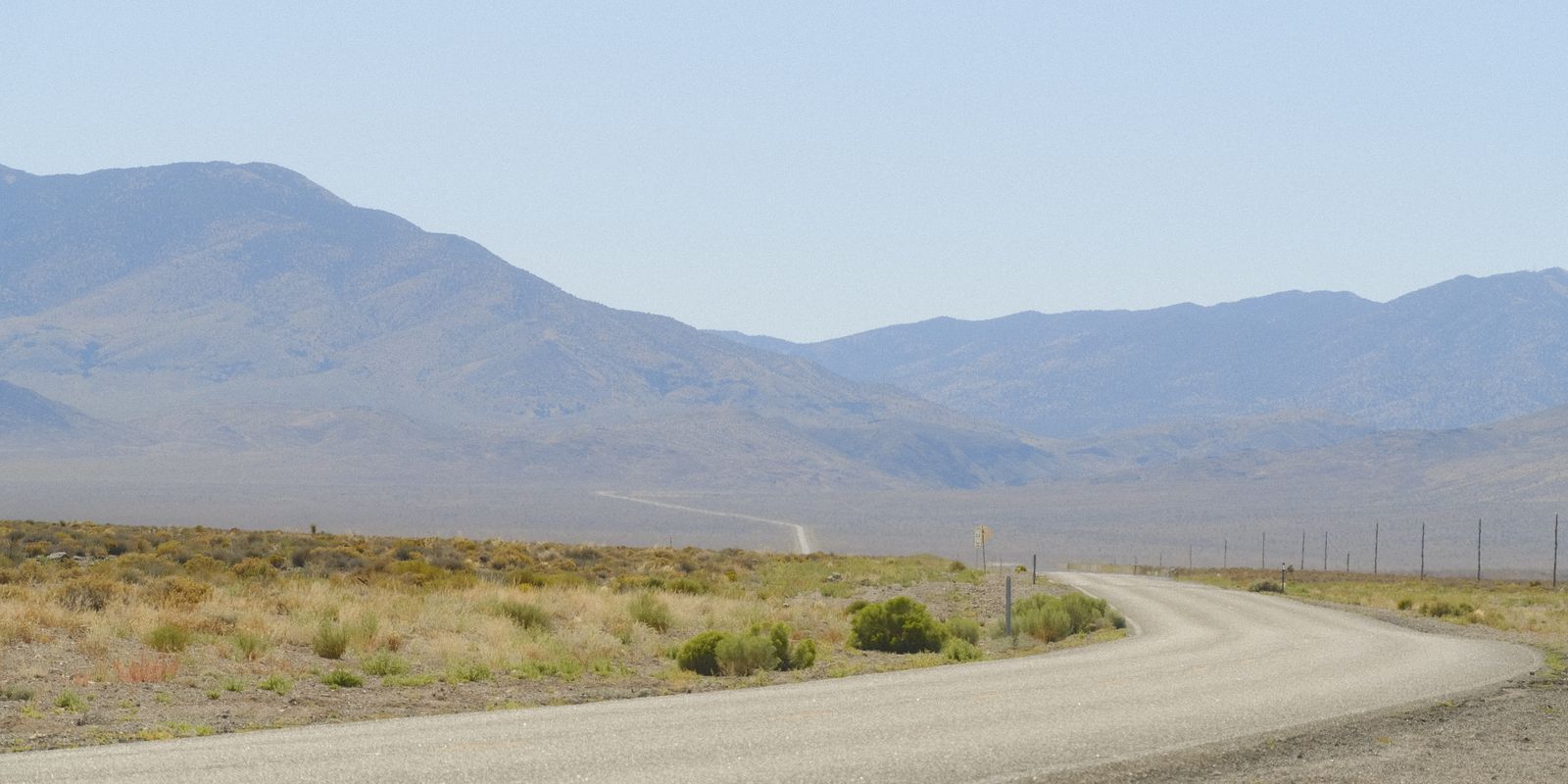 Paved road curving across a sagebrush valley toward bare desert mountains