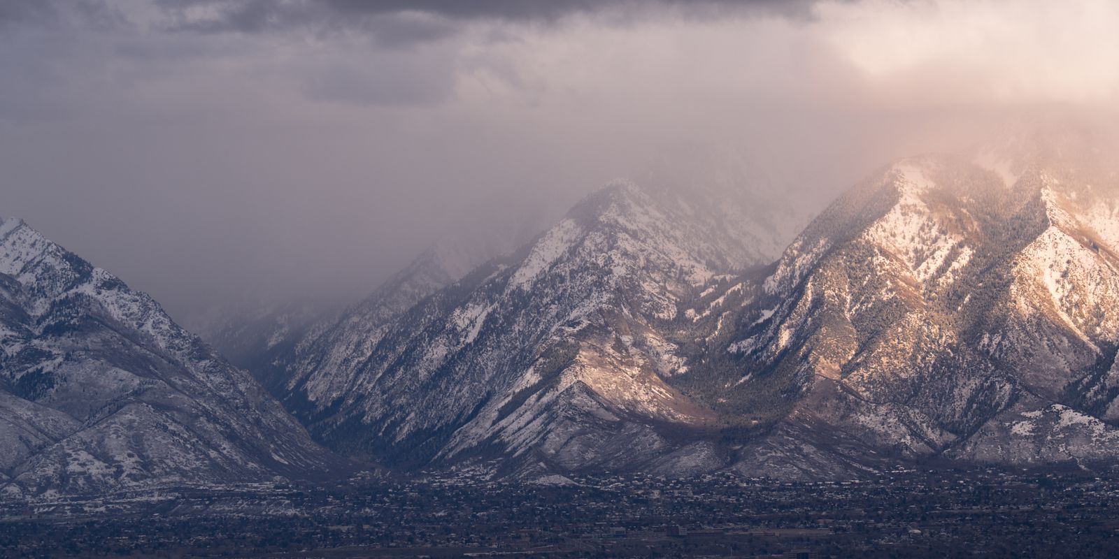 Snow-covered mountain range lit pink and gold at sunset under heavy storm cloud