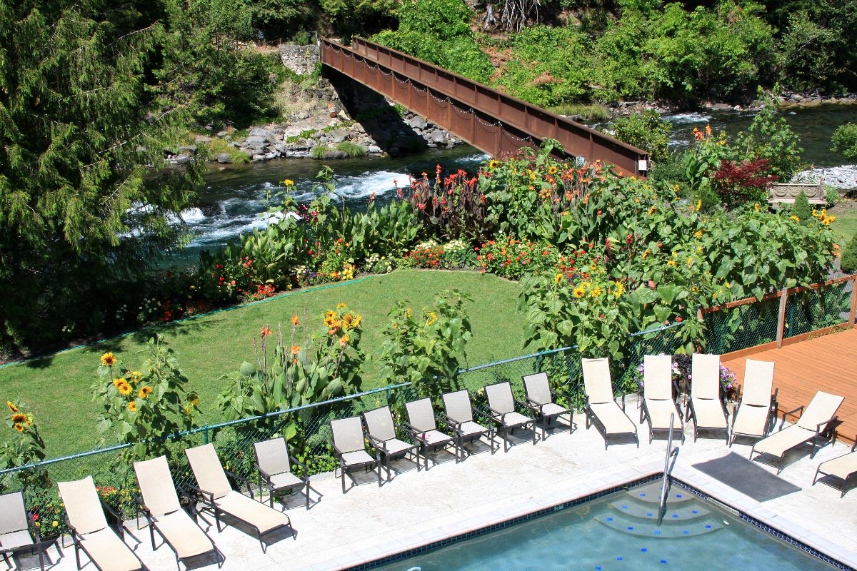 Mineral pool and loungers below flower gardens on the McKenzie River, with a footbridge over the water