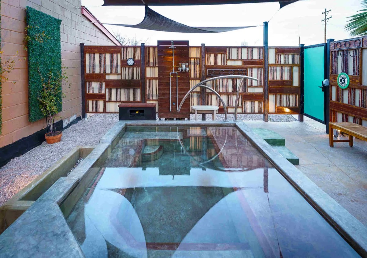 Outdoor mineral soaking tub in a fenced courtyard under a shade sail