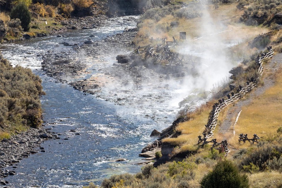 Steam rising where hot water meets the Gardner River beside a buck-and-rail fence and riverside path