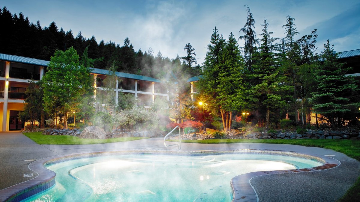 Steaming mineral pool in a landscaped courtyard surrounded by hotel wings and tall firs at dusk