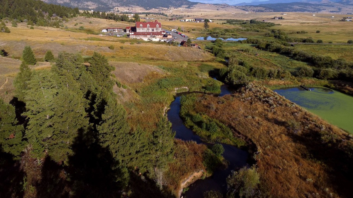 Aerial view of the Boulder Hot Springs inn above a winding creek and ponds in open Montana valley country
