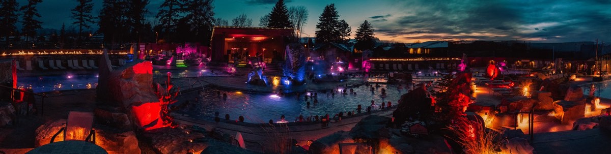 Bozeman Hot Springs' outdoor pools at dusk, lit pink and blue, with rock features and a stage