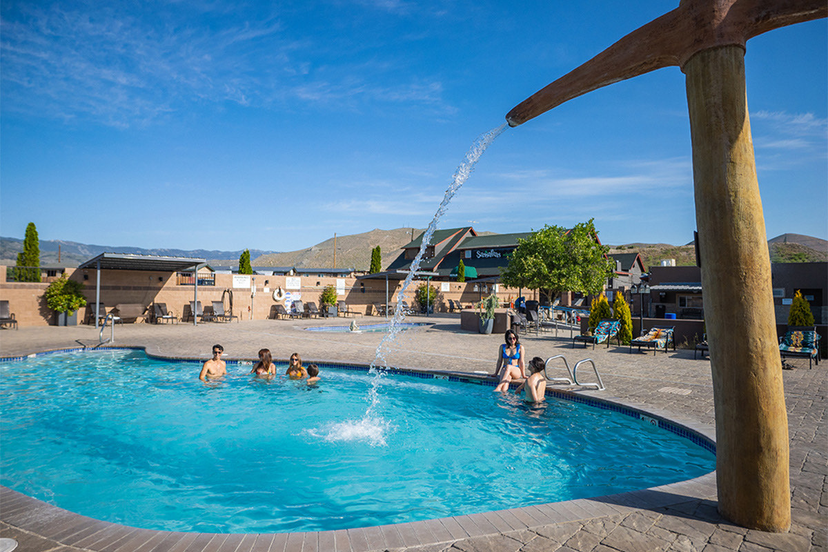 Large outdoor mineral pool with a fountain arcing from a timber post, a few soakers small in the distance