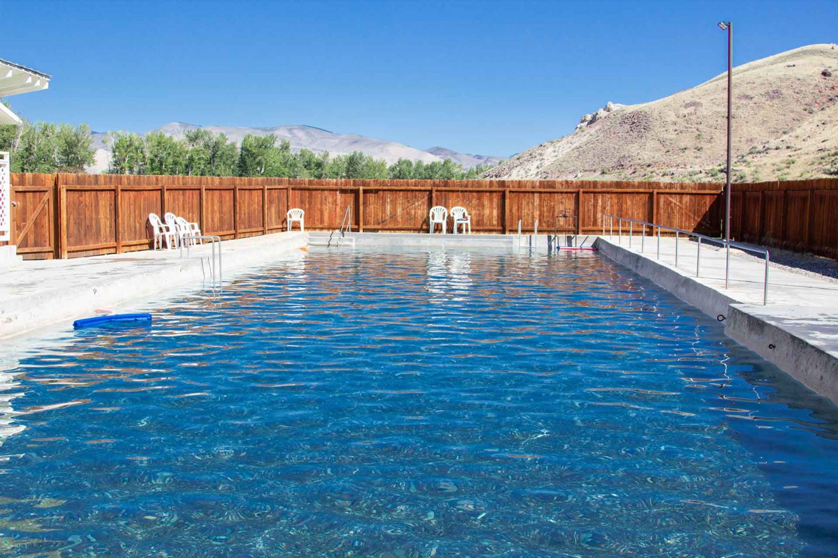 Challis Hot Springs' outdoor pool with a wooden fence and dry Idaho hills behind