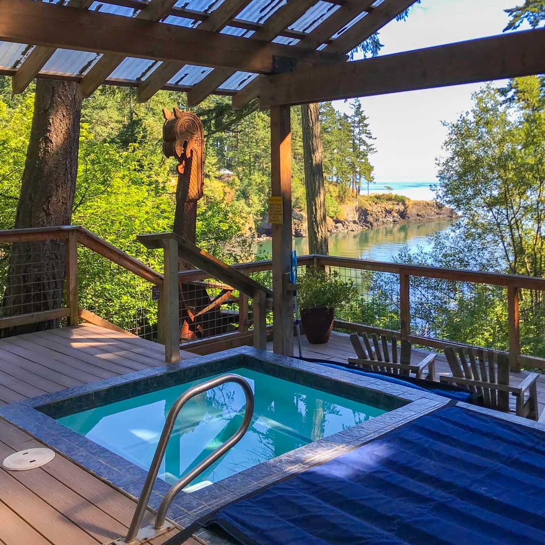 Doe Bay's deck soaking tub under a pergola, overlooking the water through trees