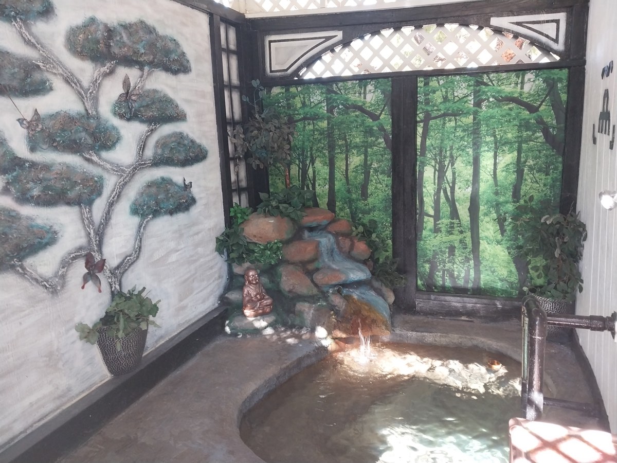 Private soaking tub at Essence of Tranquility with rock waterfall and forest mural