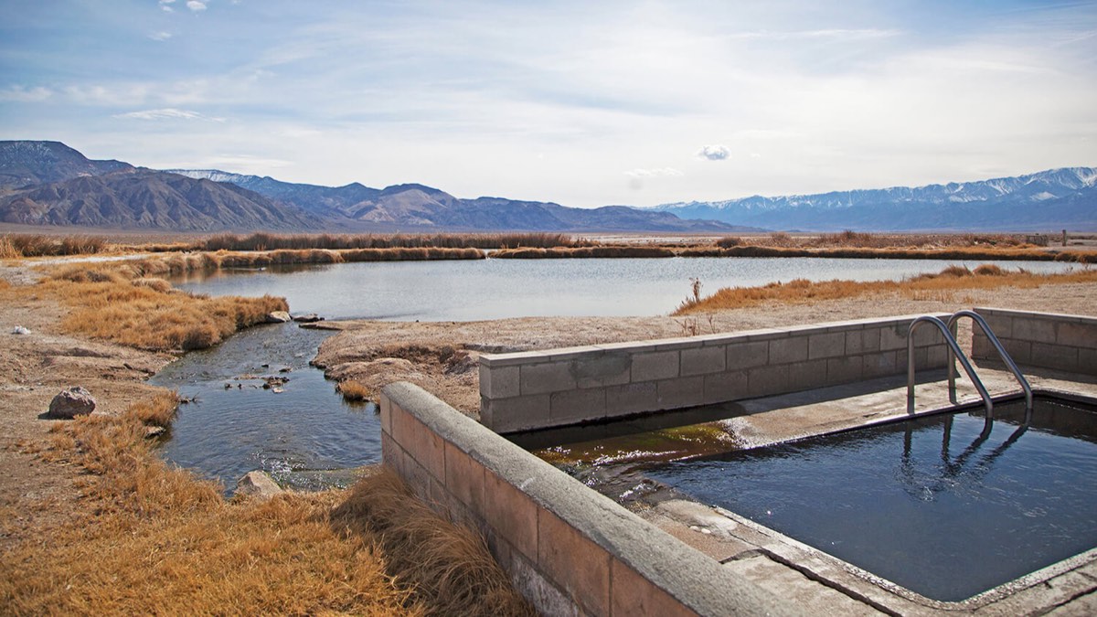 Concrete soaking tub at Fish Lake Valley with overflow pond and White Mountains behind