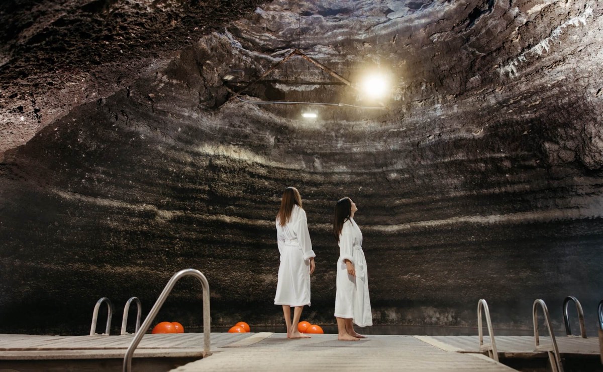 Two people in white robes on the dock inside the Homestead Crater's limestone dome, looking up