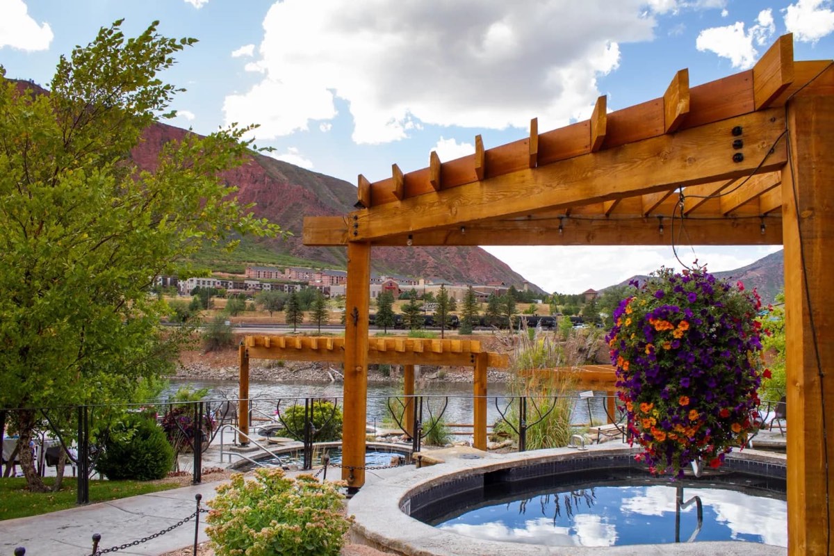 Round soaking pool under a timber pergola beside the Colorado River, red canyon walls behind