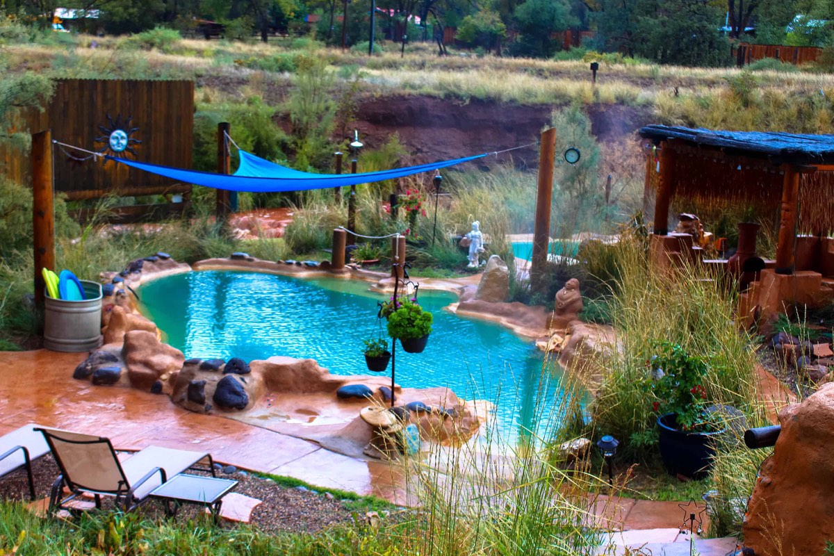 Turquoise rock-edged soaking pool among grasses, statues and a wooden shade structure