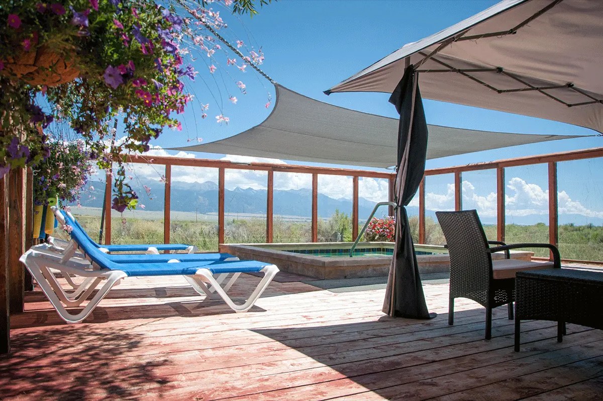 Sun deck with loungers and a hot tub under shade sails, mountains across the San Luis Valley