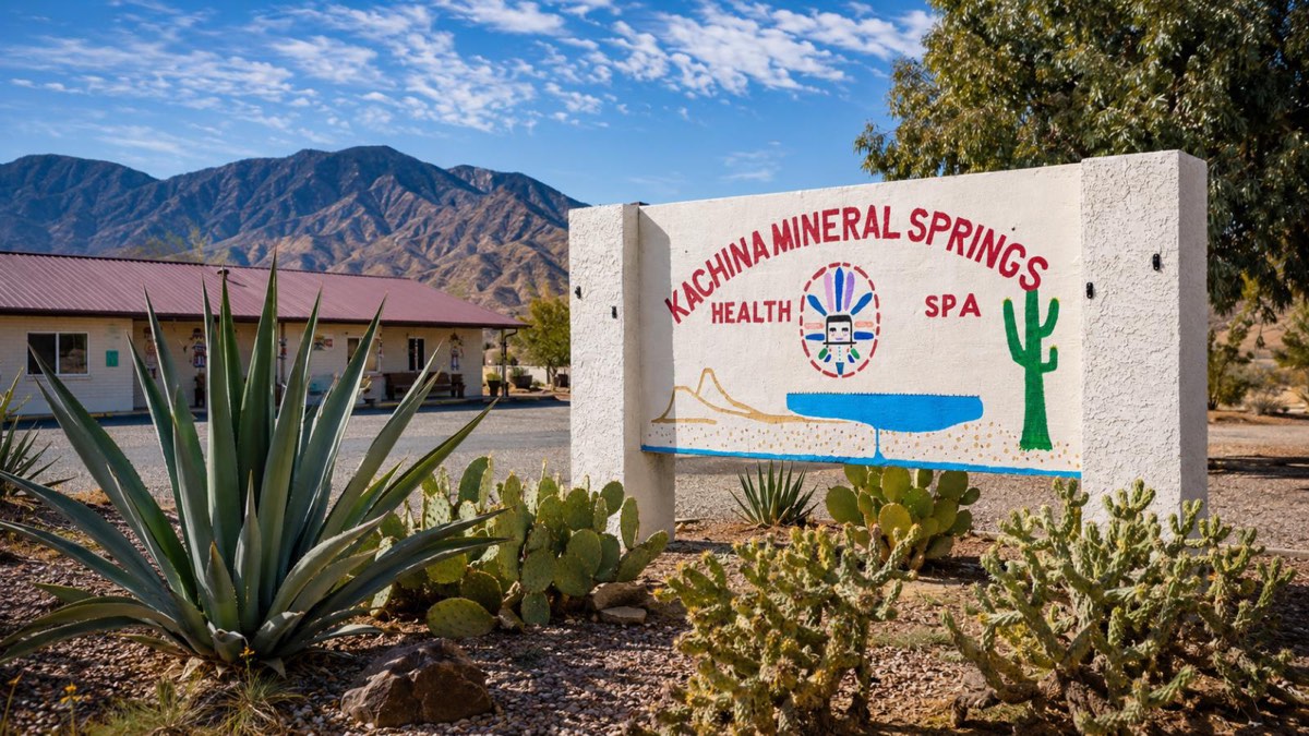 Painted Kachina Mineral Springs sign among cactus, the spa building and mountains behind