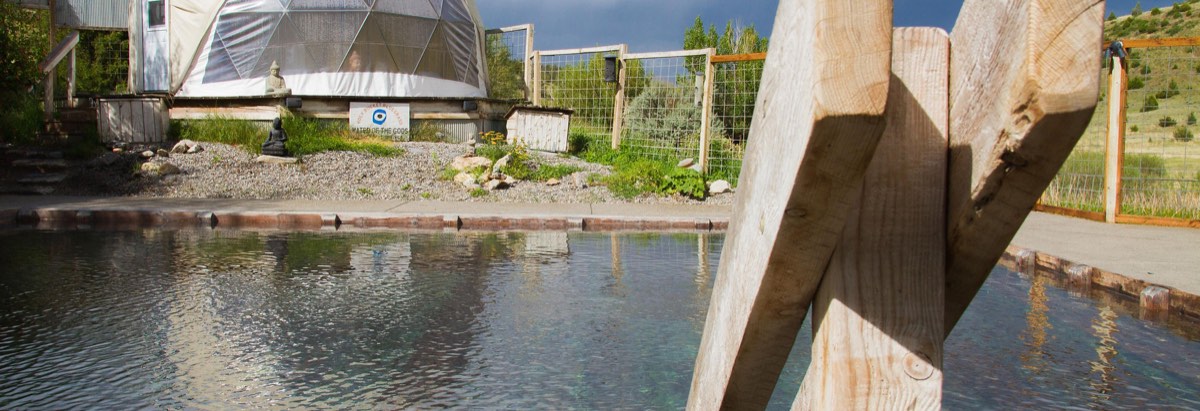 Norris Hot Springs' plank-edged soaking pool, with the geodesic stage dome and a Water of the Gods sign behind