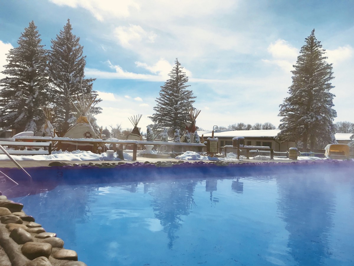 Steam rising off the outdoor mineral pool at Saratoga Hot Springs Resort, with teepees and snowy pines behind