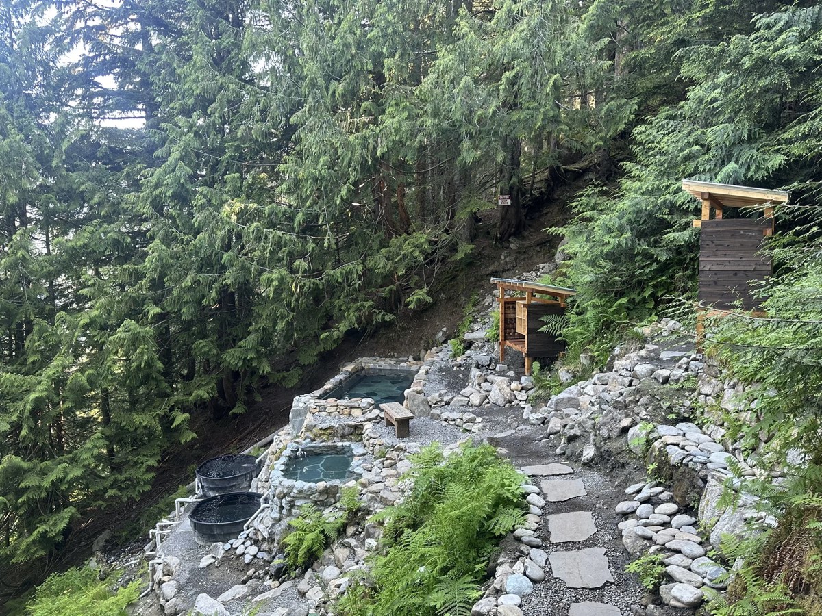 Stone-walled soaking pools terraced into a forested hillside, with wooden changing shelters above