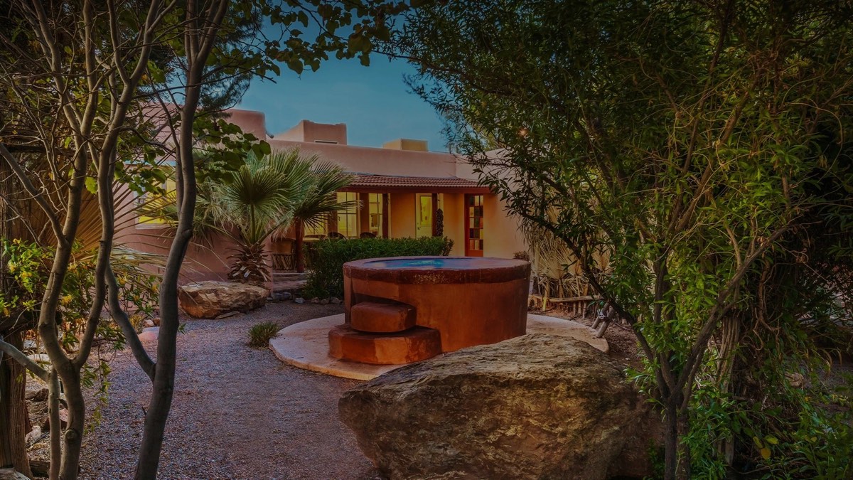 Round adobe-red outdoor soaking tub in a garden courtyard in front of the lodge at dusk