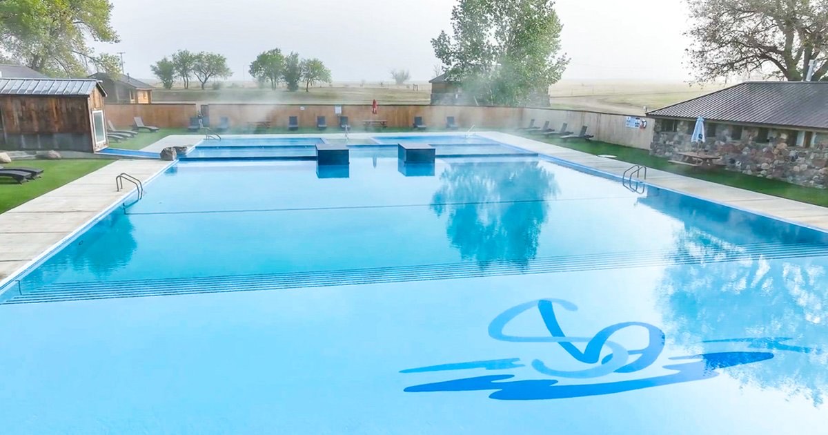 Large steaming outdoor pool under morning mist on the Montana prairie, outbuildings around it