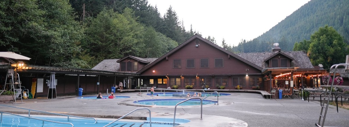Round mineral pools on a deck in front of the timber resort lodge, forested mountain behind