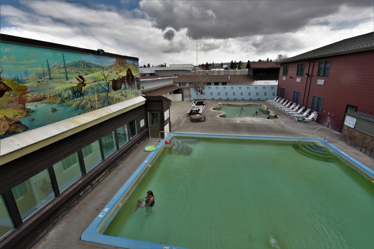Green outdoor hot pool and a smaller soaking pool behind it, beside the motel and its wildlife mural