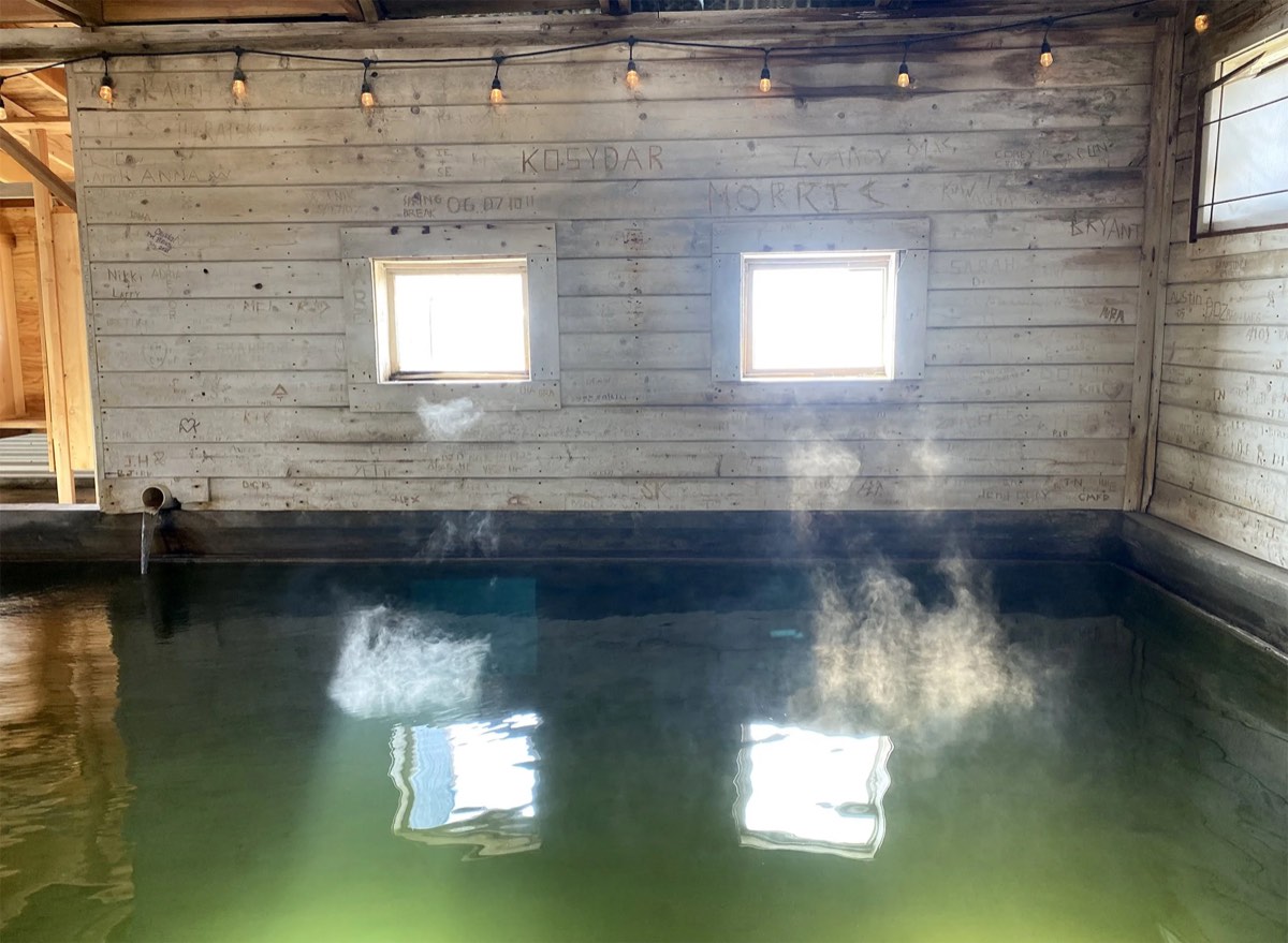 Steaming green indoor pool inside the weathered wooden bathhouse, light from two small windows