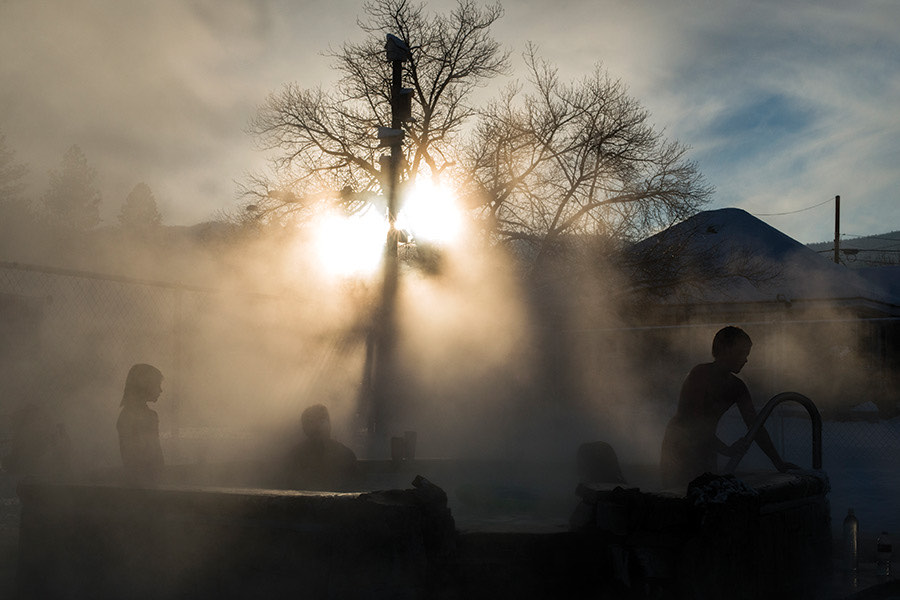 Steam rising off the outdoor hot pools at sunrise, bare trees and silhouetted soakers