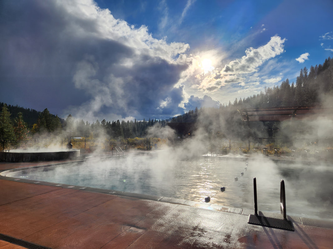 Steam rising off the outdoor soaking pool under a big sky, pine forest behind