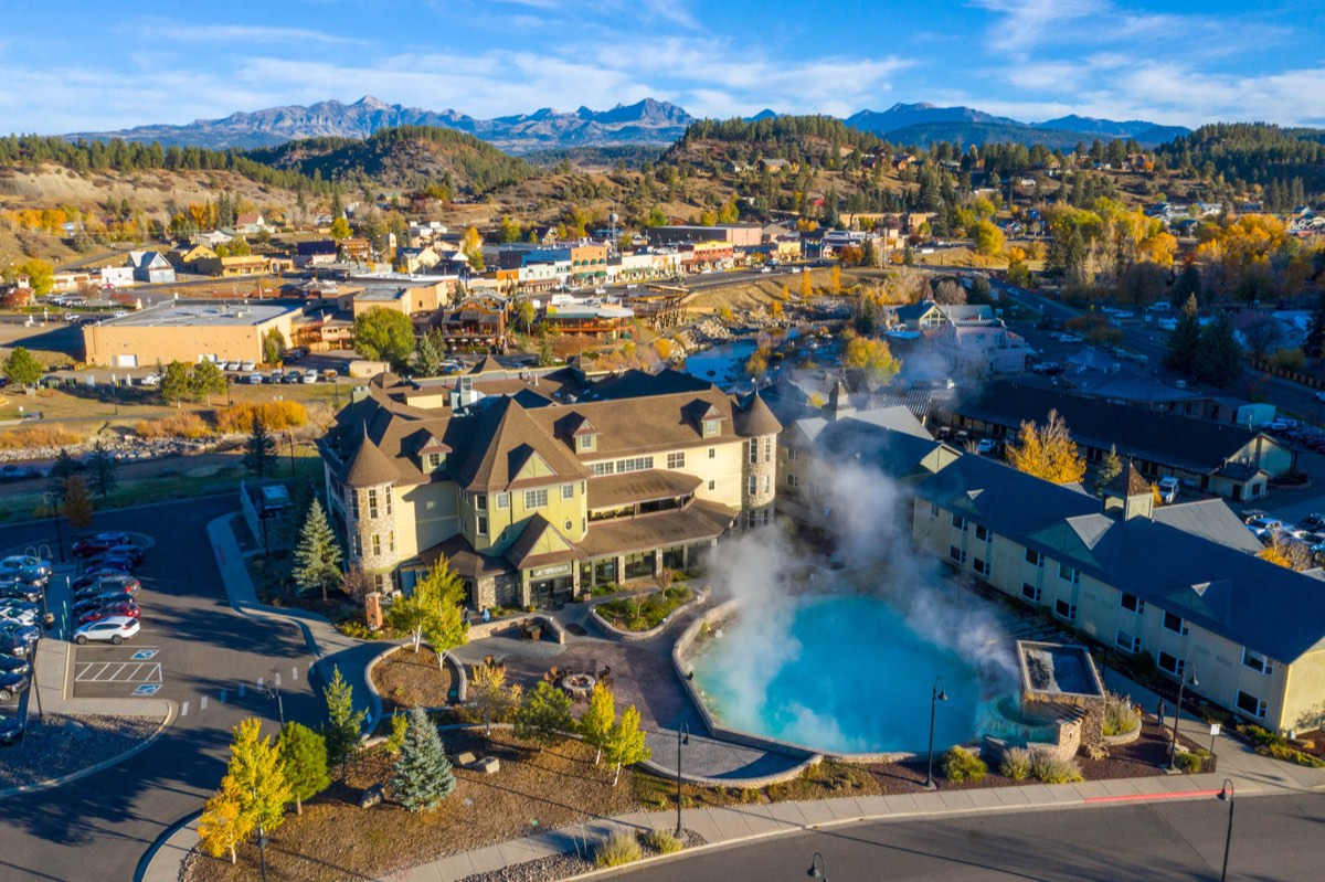 Aerial view of the resort's steaming blue Mother Spring pool beside the hotel, town and peaks behind
