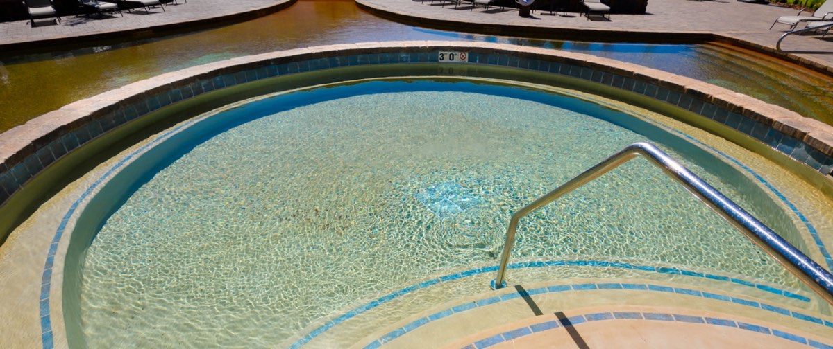 Round tiled hot pool with a handrail, the larger main pool curving behind it